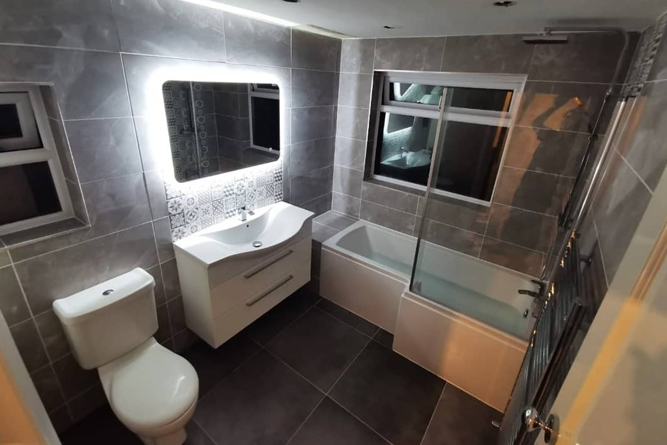 Completed bathroom with grey tiling, backlit mirror and patterned splashback