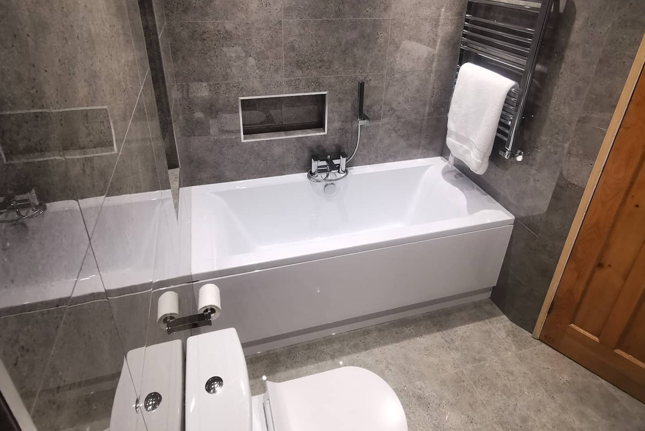 Completed bathroom with bath, chrome towel rail and a tiled recess