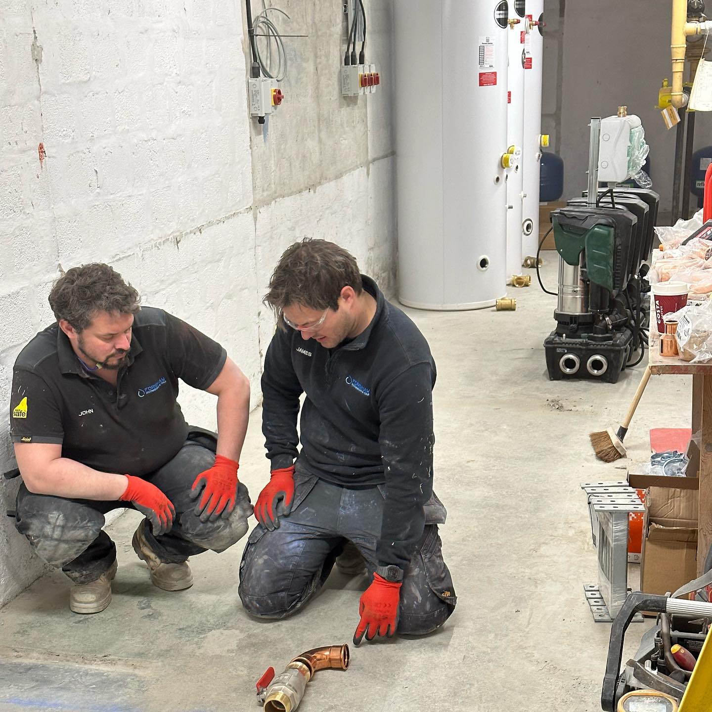 John and James of Forshaw Water and Gas in a plant room, with unvented cylinders behind them